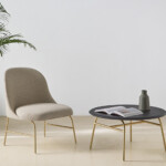 Indoor space with cream lounge chair aside a small table decorated with a book and a vase.