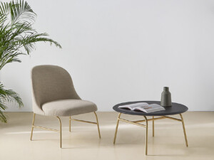 Indoor space with cream lounge chair aside a small table decorated with a book and a vase.